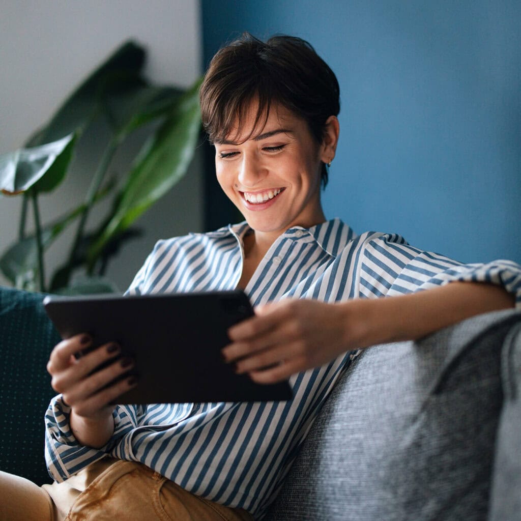 Lächelnde Frau mit Tablet auf Sofa – effizientes Immobilienmanagement durch stabile Glasfaserverbindung mit AVACOMM