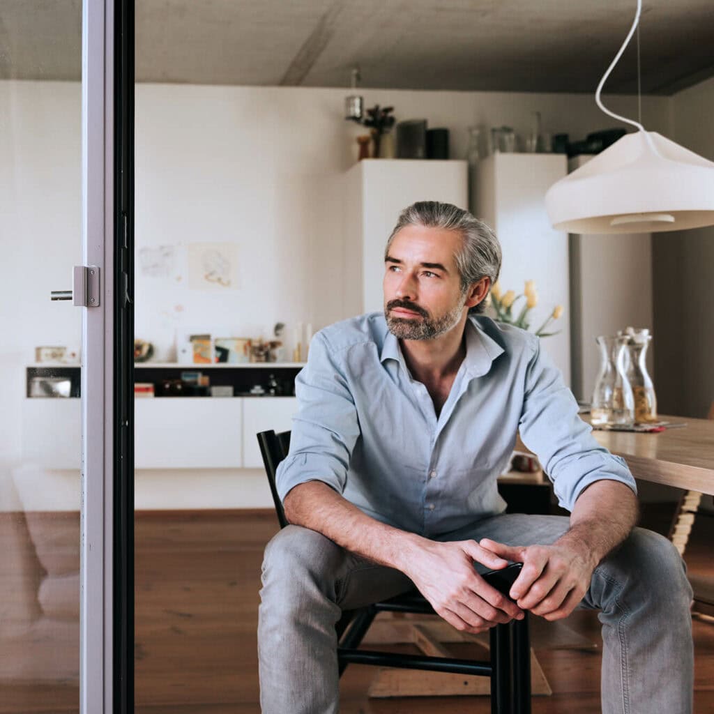 Mann sitzt nachdenklich in moderner Küche – nachhaltige Energieversorgung und Glasfaserinfrastruktur für Wohnobjekte mit AVACOMM
