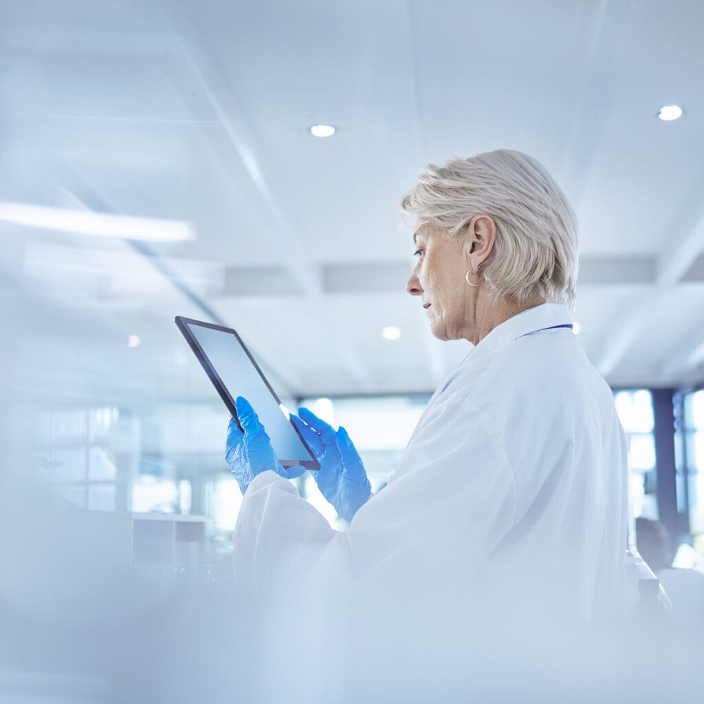 Labortechnikerin betrachtet auf dem Tablet, das Sie in den Händen hält, die Datenanalyse in Echtzeit, Glasfaser macht es möglich.